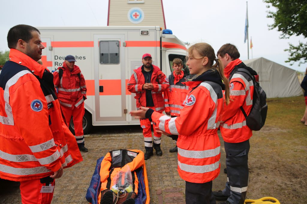 Eine Gruppe Menschen in leuchtend-roter Uniform steht um eine Puppe herum.