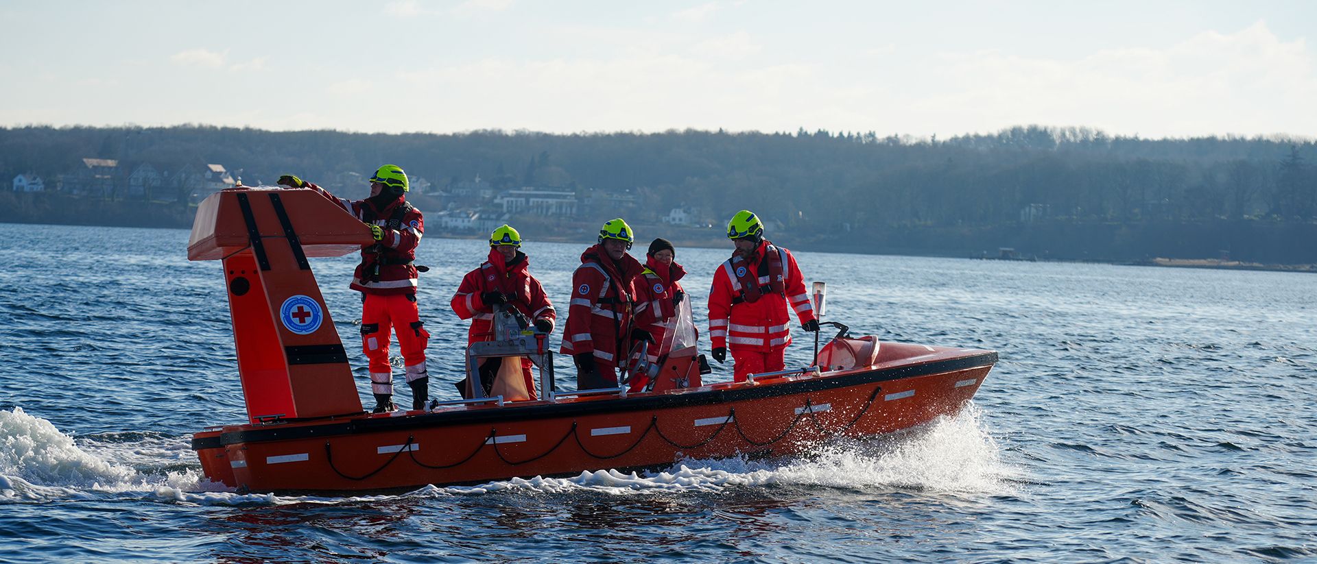An Bord eines orangefarbenen Rettungsbootes überqueren 5 Personen in DRK-Einsatzkleidung die Flensburger Förde.