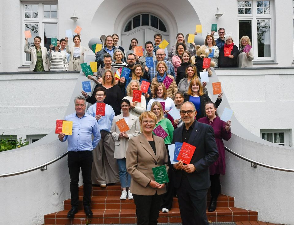 Gruppenfoto: Rund 40 Menschen stehen auf einer Treppe und halten bunte Karten in die Luft.