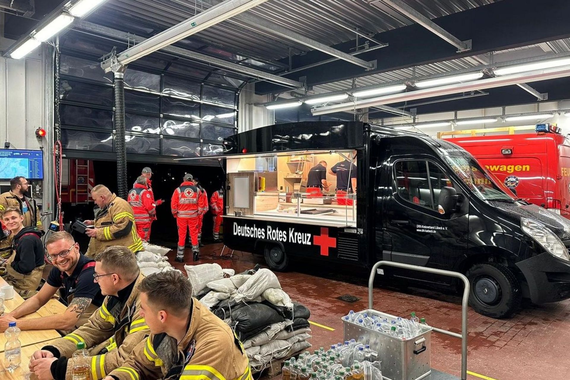 Etwa ein Dutzend Einsatzkräfte stärkt sich an einem Imbisswagen des Deutschen Roten Kreuzes.