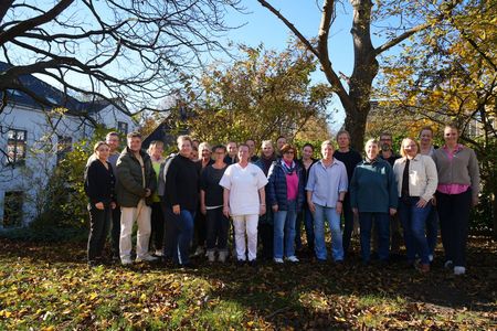 Gruppenfoto: 23 Personen stehen vor einer Hecke.