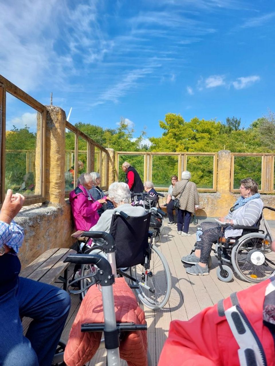 Ausflug in den Grömitzer Zoo Eine Gruppe Senio*innen, teilweise mit Rollstühlen und Rollatoren, verweilt auf einer hölzernen Terrasse.