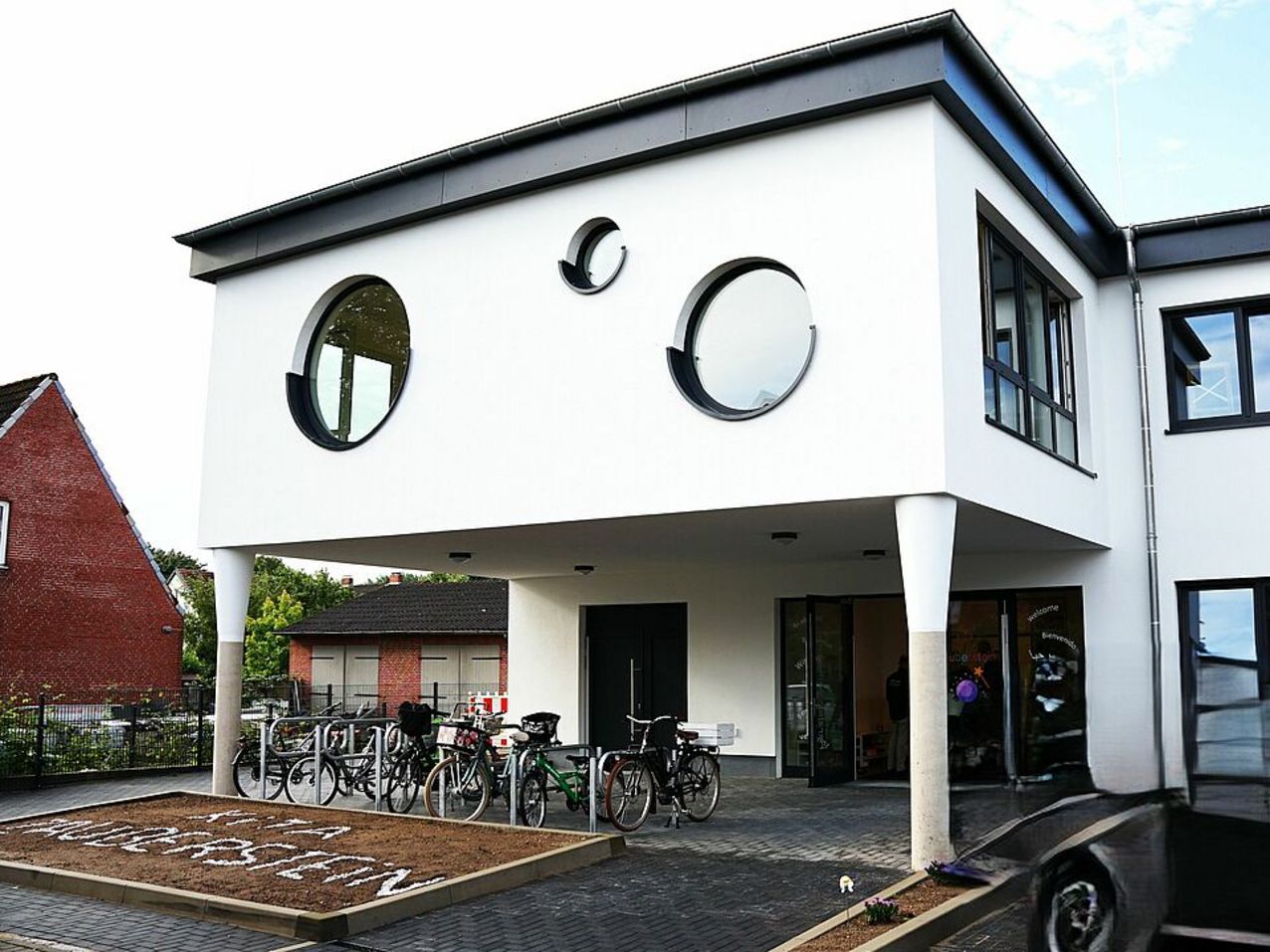 Blick auf ein zweigeschossiges weißes Gebäude. Im Obergeschoss hat es 3 runde Fenster.
