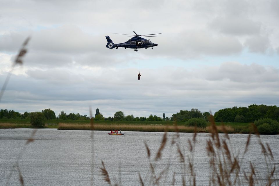 Ein Hubschrauber steht über einem Fluss in der Luft. Dazwischen hängen zwei Luftretter*innen an einem Seil, die gerade wieder an Bord gezogen werden.