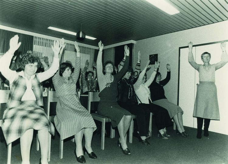 Eine Gruppe Frauen übt Gymnastik auf dem Stuhl aus