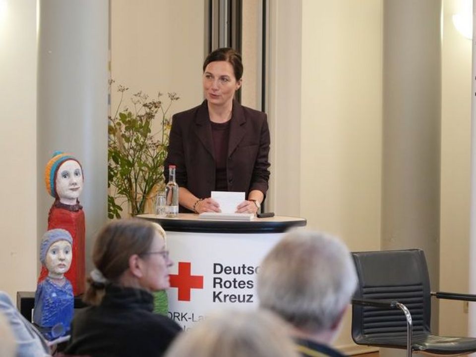 Eine Frau steht an einem Rednerpult und spricht zu ihrem Publikum vor sich.