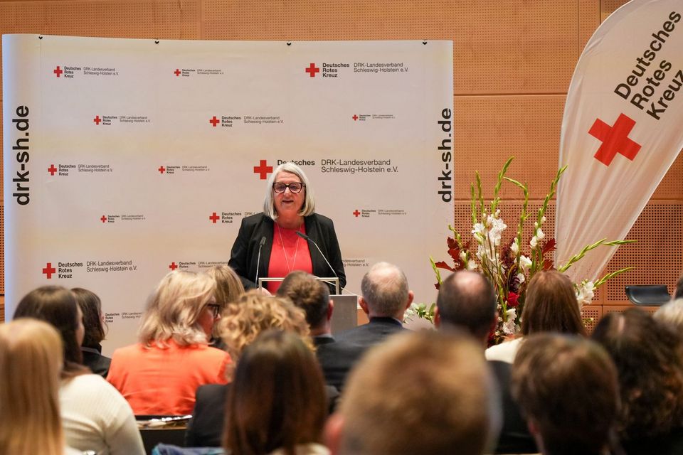 Dr. Dorit Stenke auf dem Parlamentarischen Abend des DRK SH Eine Frau steht an einem Rednerpult und spricht zu einigen Menschen.