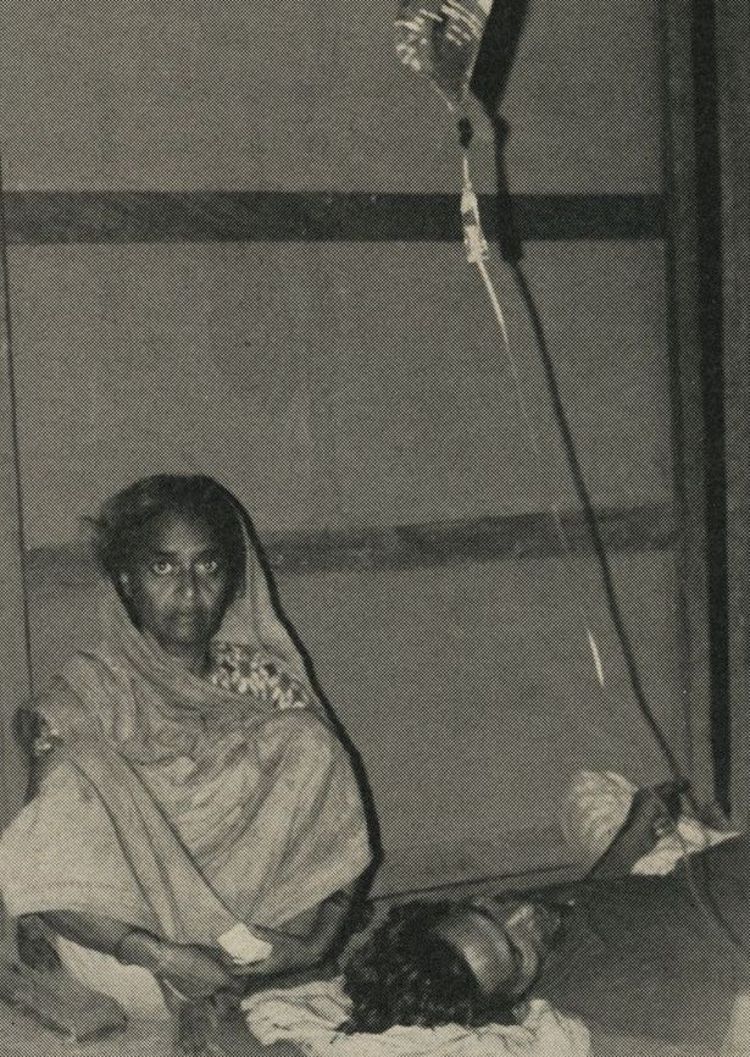 Eine Frau sitzt bei einem Mann der eine Infusion bekommt