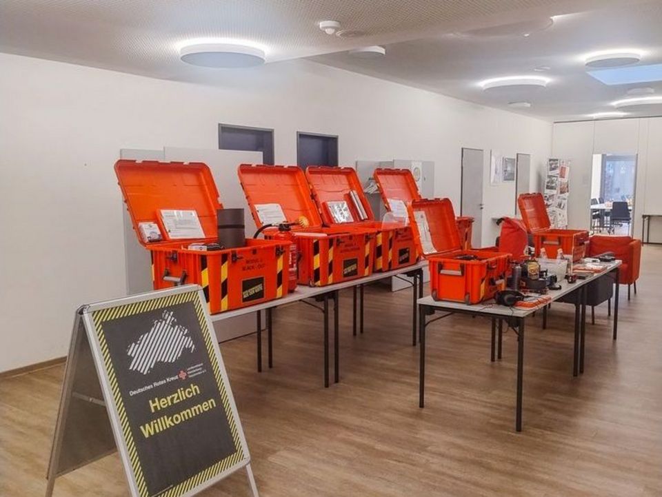 Sechs große rote Kunststoffkisten stehen aufgeklappt auf mehreren Tischen.