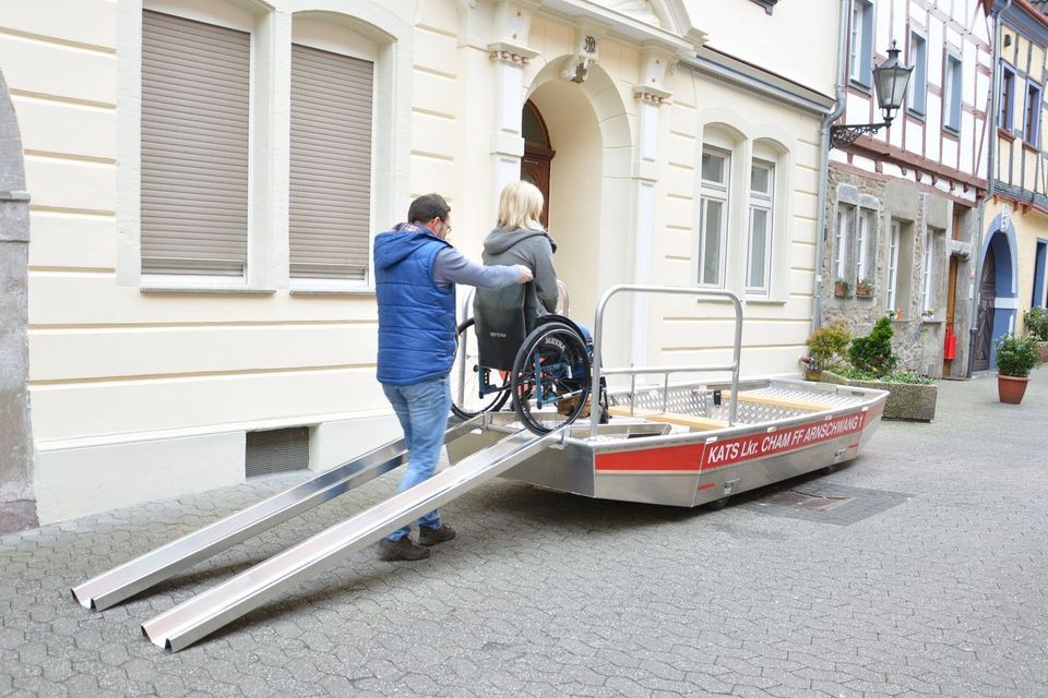 Ein Mann schiebt eine Frau im Rollstuhl über eine Rampe auf ein Rettungsboot.