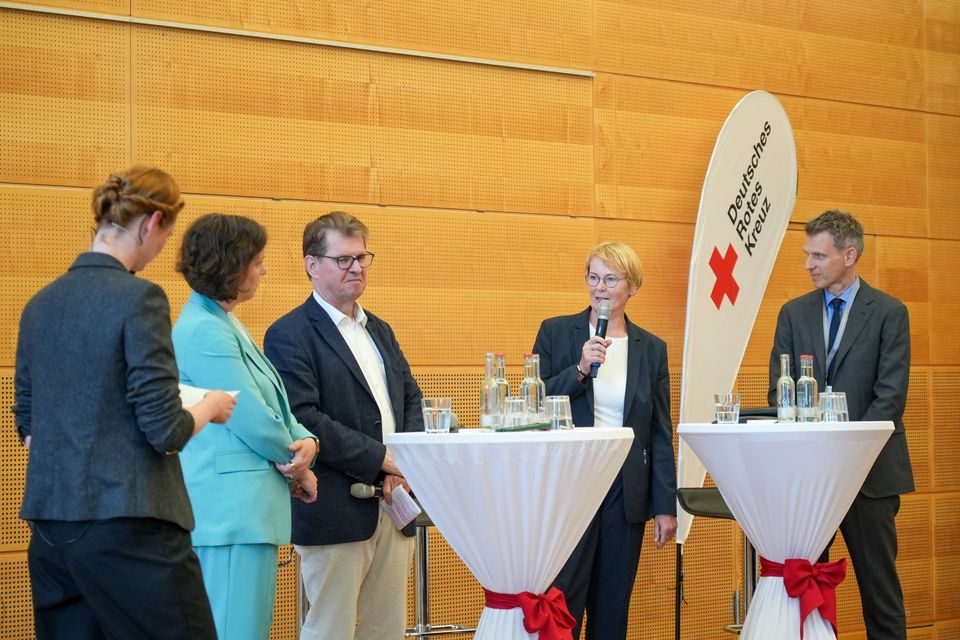 Fünf Menschen stehen um zwei Stehtische herum auf einer Bühne und diskutieren.