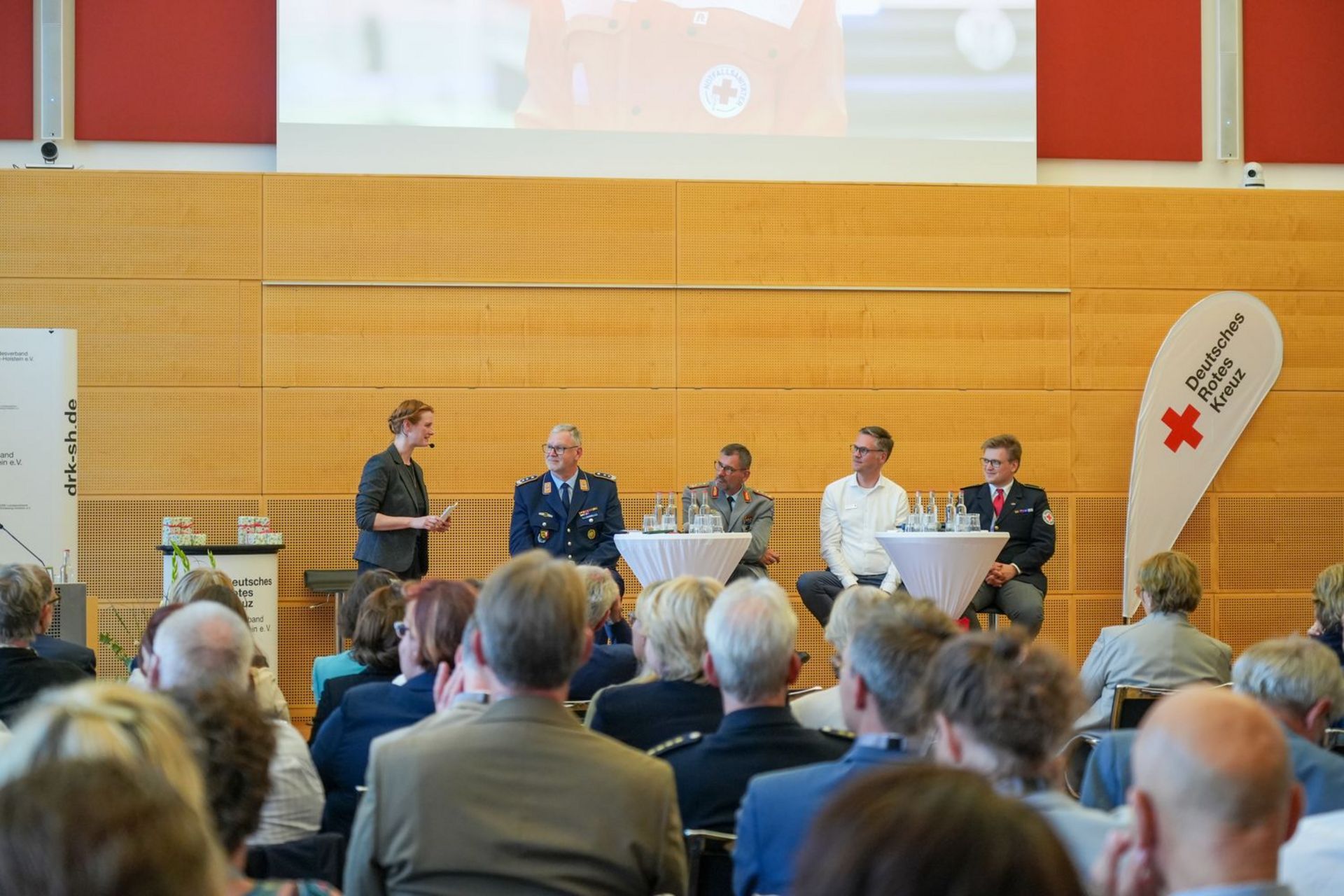 Fünf Menschen diskutieren auf einer Bühne vor großem Publikum im Vordergrund.