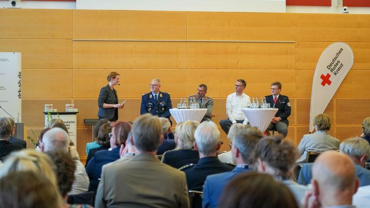Fünf Menschen diskutieren auf einer Bühne vor großem Publikum im Vordergrund.