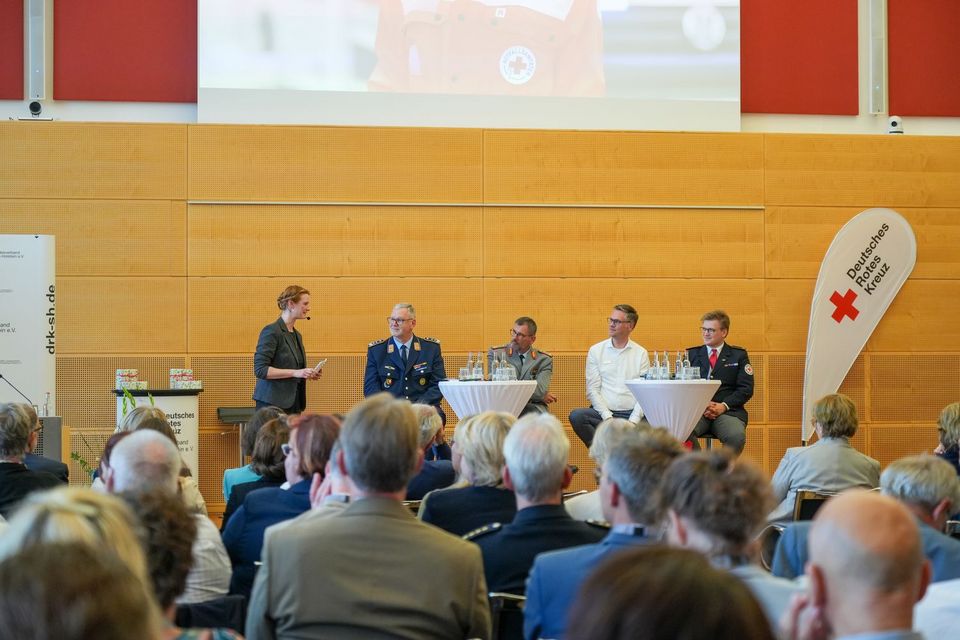 Fünf Menschen diskutieren auf einer Bühne vor großem Publikum im Vordergrund.