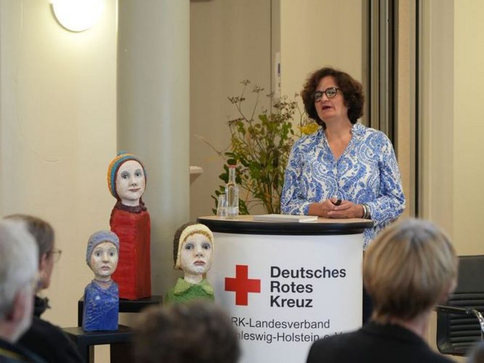 Eine Frau steht an einem Rednerpult und spricht zu ihrem Publikum vor sich.