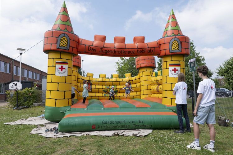 Auf einer großen Hüpfburg spielen vier Kinder. Auf der Hüpfburg steht geschrieben: Das Jugendrotkreuz hebt ab. Gesponsert von der Kreissparkasse Pinneberg.