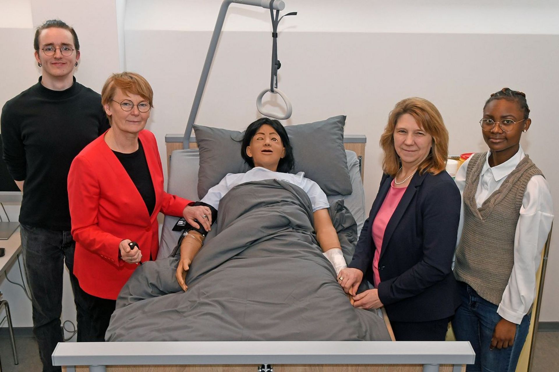 4 Personen stehen um ein Krankenbett, in dem eine Übungspuppe liegt.