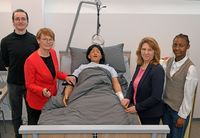 4 Personen stehen um ein Krankenbett, in dem eine Übungspuppe liegt.