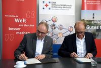 Zwei Personen sitzen an einem Tisch und unterschreiben Dokumente.