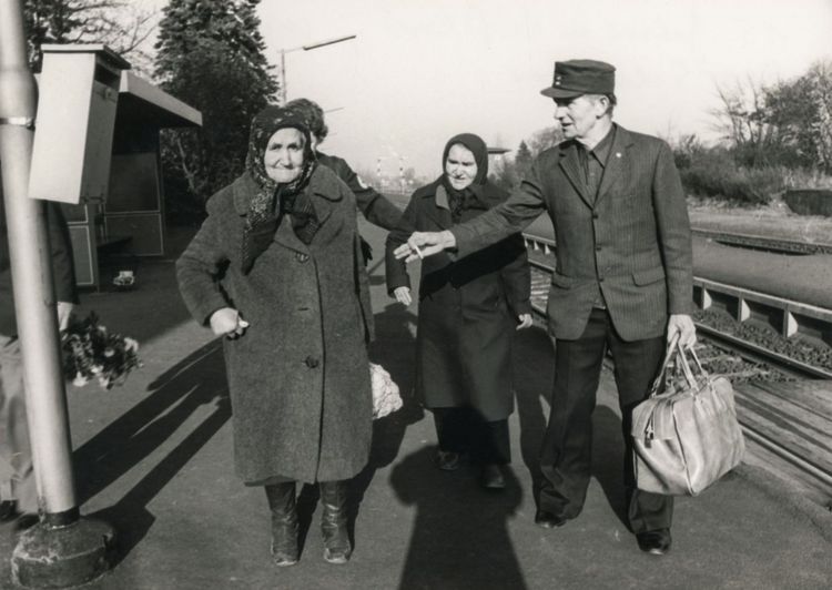 Drei ältere Menschen an einem Bahnhof