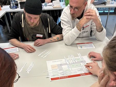 Vier Personen sitzen an einem Tisch und spielen ein Planspiel.