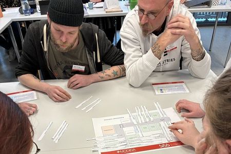 Vier Personen sitzen an einem Tisch und spielen ein Planspiel.