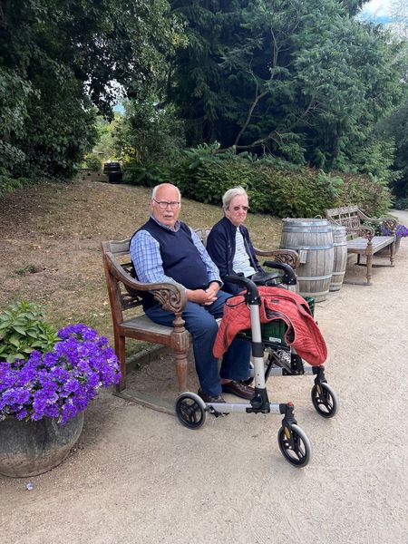 Zwei Senior*innen sitzen auf einer hölzernen Bank in einem grünen Park.