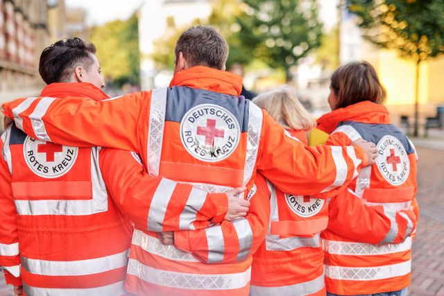 Symbolfoto: Vier Ehrenamtliche in Einsatzbekleidung von hinten fotografiert