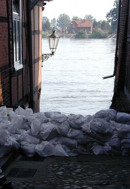 Gestapelte Sandsäcke zwischen zwei Häusern, im Hintergrund die Elbe