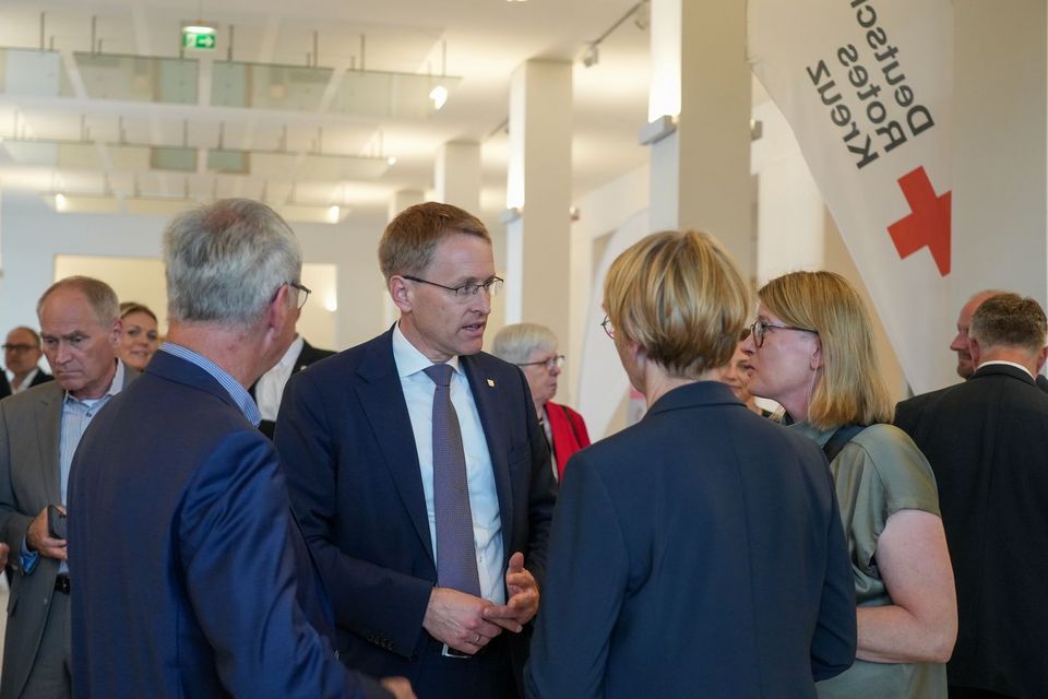 Vier Menschen unterhalten sich in einem großen Saal voller Menschen.