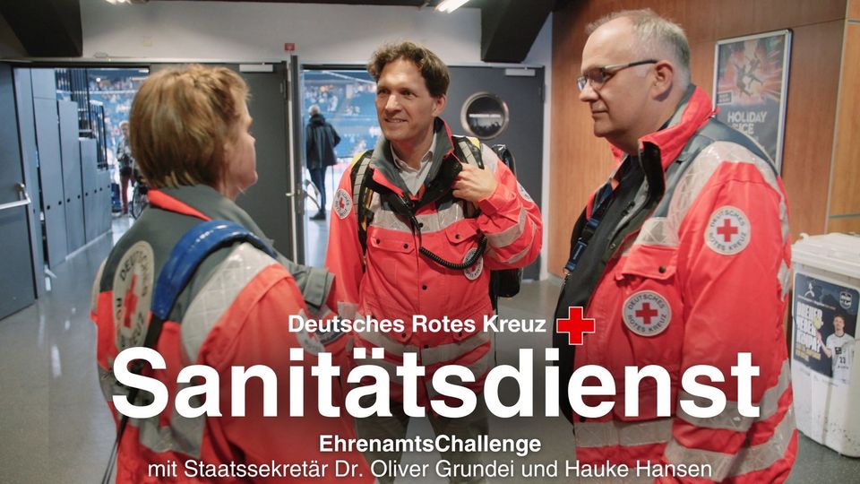 3 Menschen in orangefarbenen DRK-Einsatzjacken unterhalten sich.