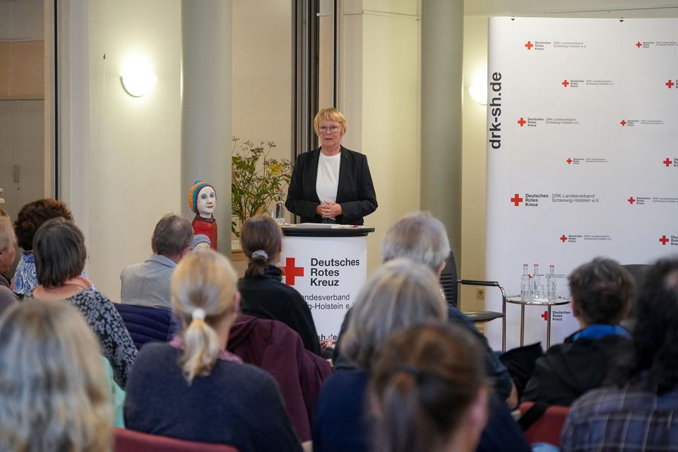 Eine Frau steht an einem Rednerpult und spricht zu ihrem Publikum vor sich.