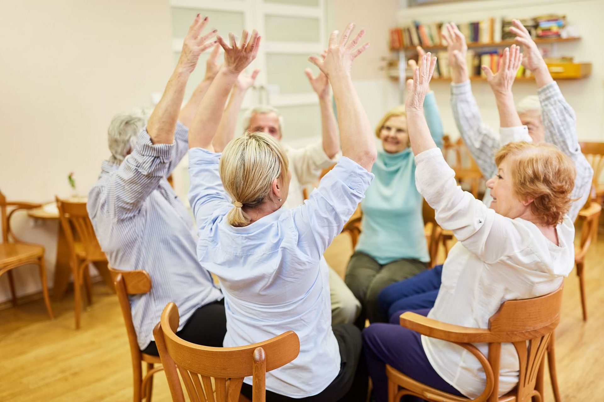 Gruppe Senioren im Altenheim sitzt im Stuhlkreis und macht Sitzgymnastik oder Bewegungstherapie.