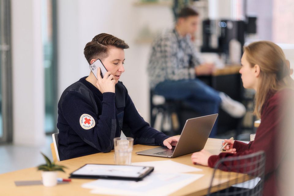 Mitarbeiterin des DRK arbeitet am Laptop und telefoniert mit einem Smartphone