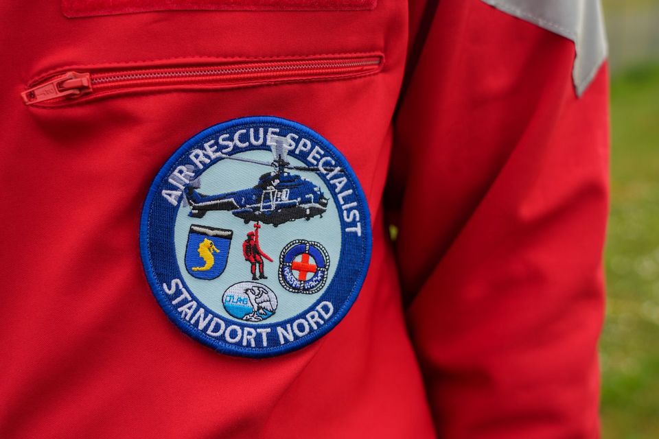 Auf dem äußeren Rand eines runden blauen Aufnähers steht in weißer Schrift: Air Rescue Specialist - Standort Nord. In der Mitte des Aufnähers ist ein blauer Hubschrauber und darunter ein roter Luftretter abgebildet. Daneben sind die Logos der Seepferdchenflieger der Bundespolizei, der DLRG und der DRK-Wasserwacht angeordnet.