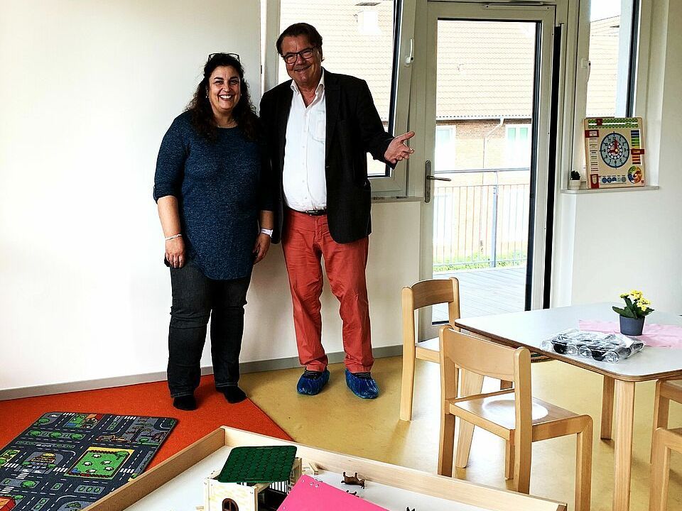 Zwei Personen stehen in einem Kita-Raum mit Spielzeugen.