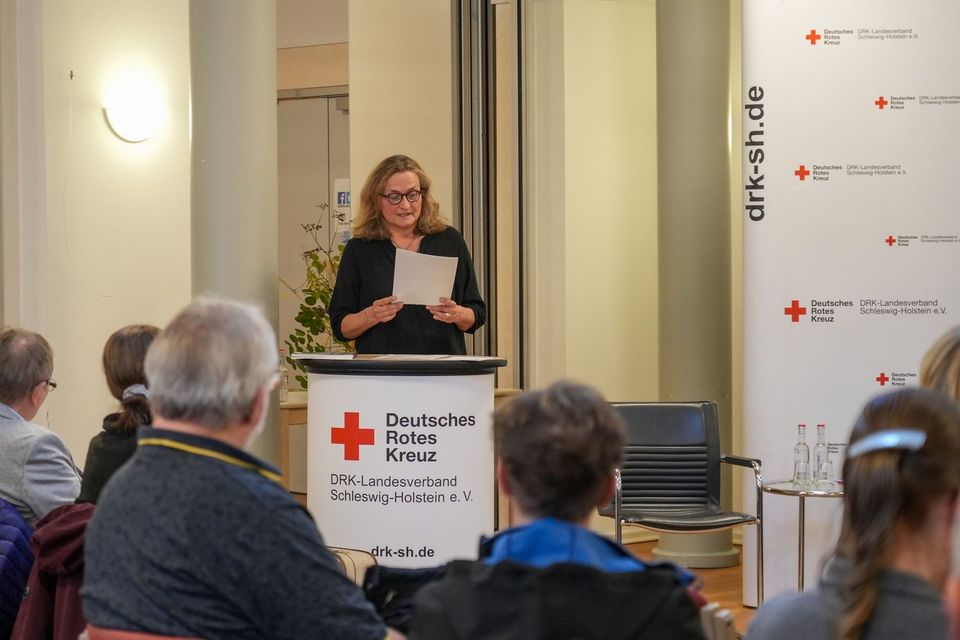 Eine Frau steht an einem Rednerpult und spricht zu ihrem Publikum vor sich.