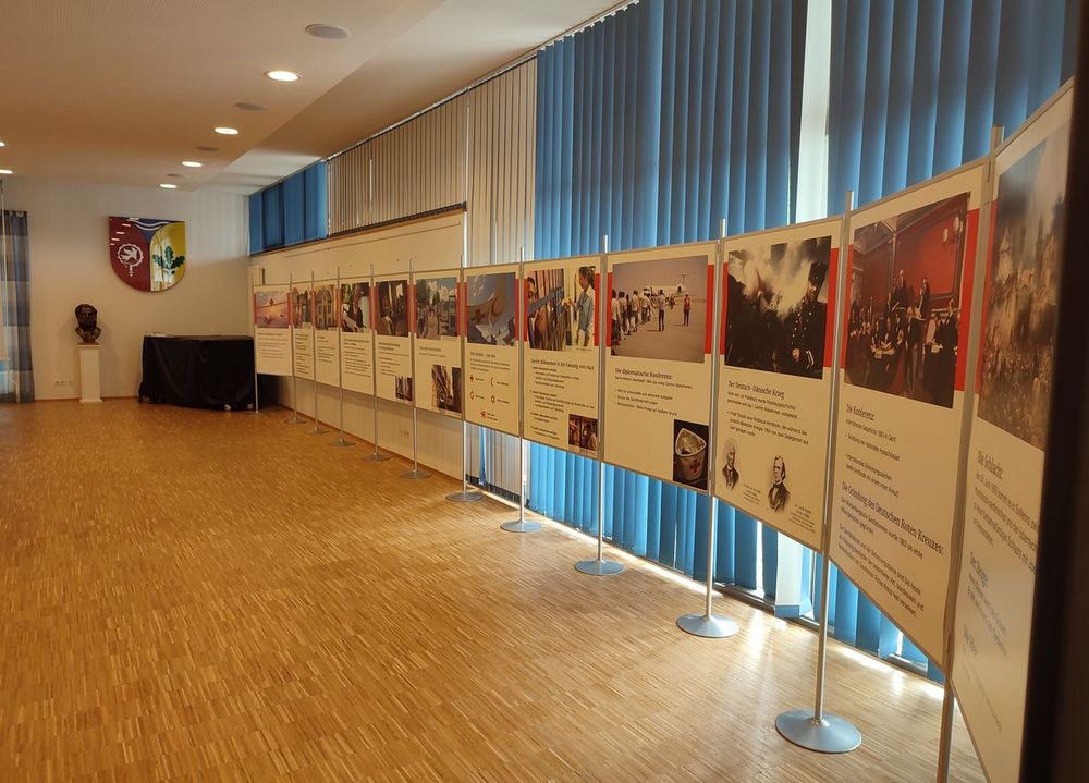 In einem großen Saal steht eine lange Reihe von großen Stellwänden. Sie zeigen die Geschichte des humanitären Völkerrechts.