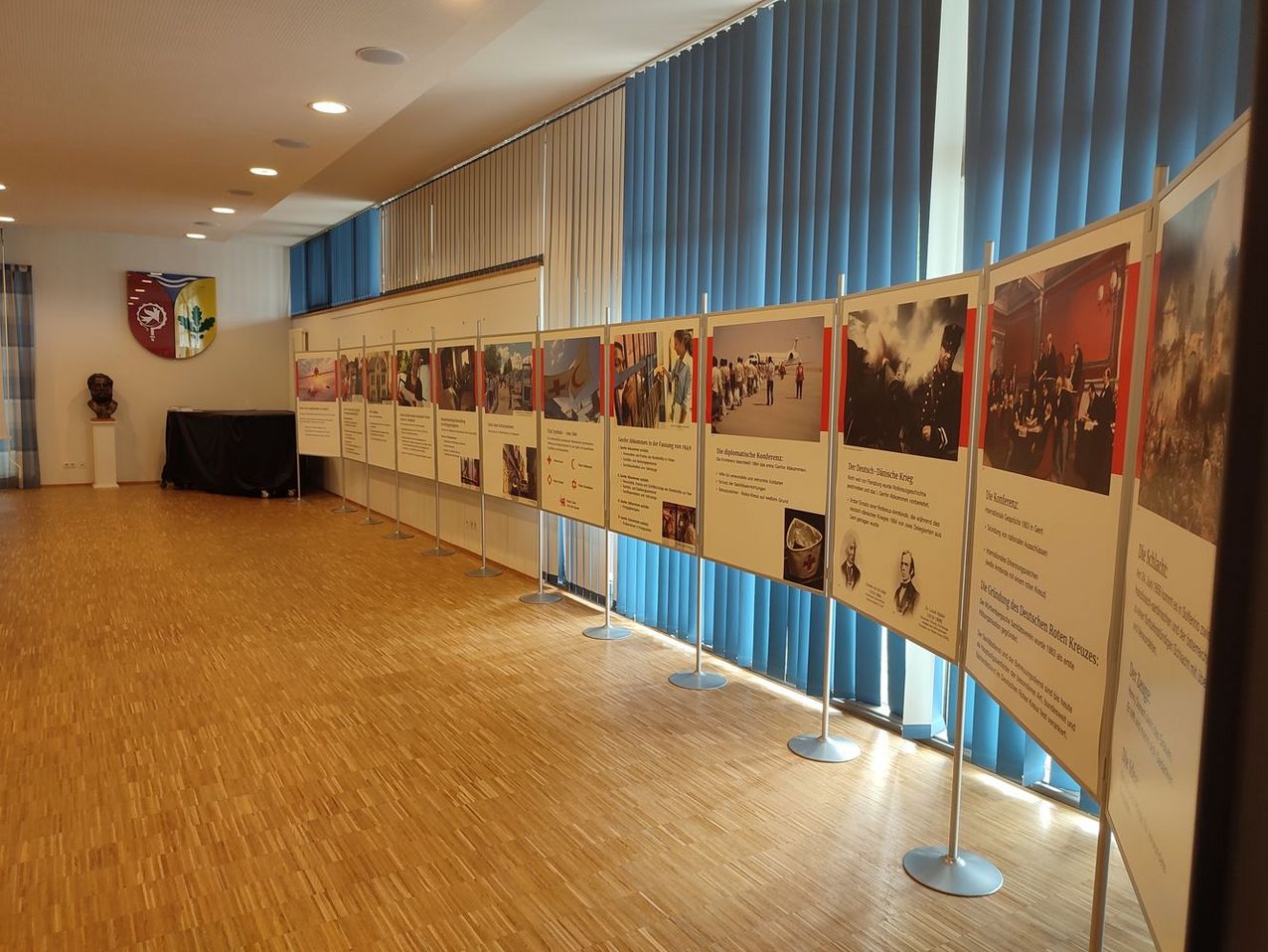 In einem großen Saal steht eine lange Reihe von großen Stellwänden. Sie zeigen die Geschichte des humanitären Völkerrechts.
